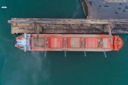Vista aérea de um navio cargueiro atracado no porto de São Francisco do Sul, com a movimentação marítima ao redor.