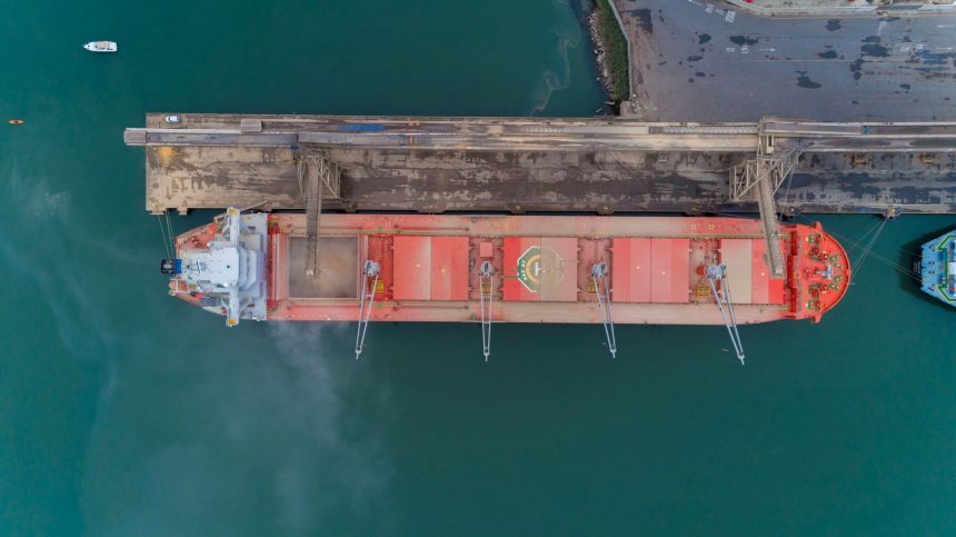 Vista aérea de um navio cargueiro atracado no porto de São Francisco do Sul, com a movimentação marítima ao redor.