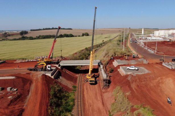 Vista aérea de uma ponte em construção, com guindastes e máquinas no canteiro de obras.