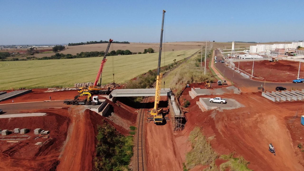 Vista aérea de uma ponte em construção, com guindastes e máquinas no canteiro de obras.