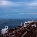 Vista aérea de um grande navio cargueiro navegando em alto-mar sob céu nublado.